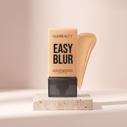 Huda Beauty Easy Blur Foundation styled on travertine pedestal, blush studio