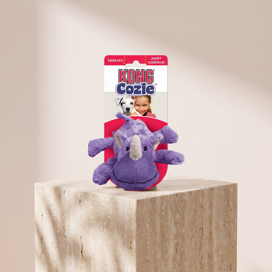 KONG Cozie Rosie Rhino squeaky plush dog toy styled on travertine pedestal, blush studio